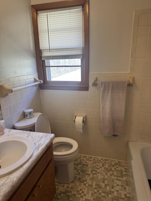 full bathroom with a wainscoted wall, toilet, tile walls, a bath, and vanity