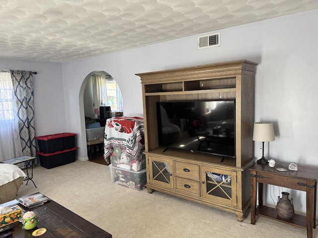 living area featuring visible vents, arched walkways, and light colored carpet