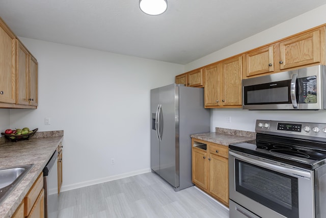 kitchen with a sink, baseboards, light floors, and appliances with stainless steel finishes