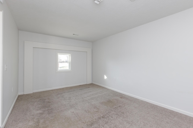 spare room featuring baseboards, carpet, and a textured ceiling