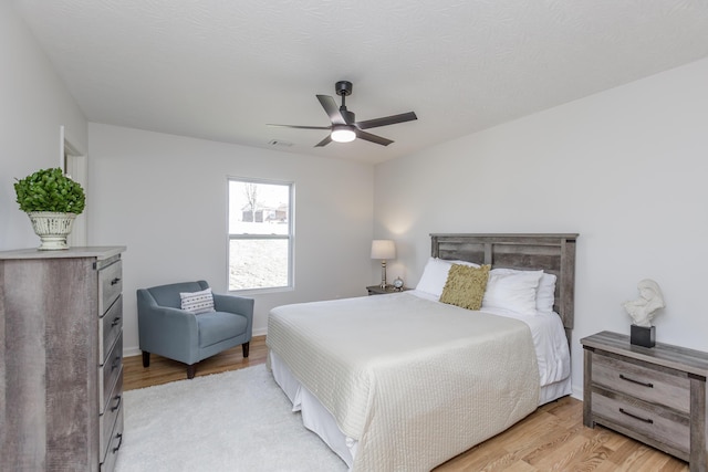 bedroom featuring light wood-type flooring, visible vents, a textured ceiling, baseboards, and ceiling fan