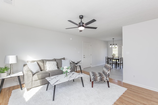 living area with visible vents, ceiling fan with notable chandelier, baseboards, and light wood finished floors