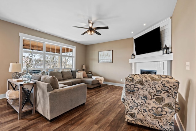 living room with a ceiling fan, baseboards, dark wood-style flooring, and a large fireplace