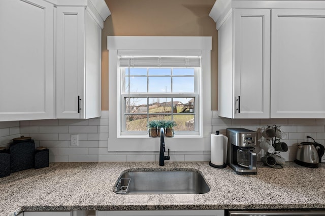 kitchen with decorative backsplash, white cabinets, light stone countertops, and a sink