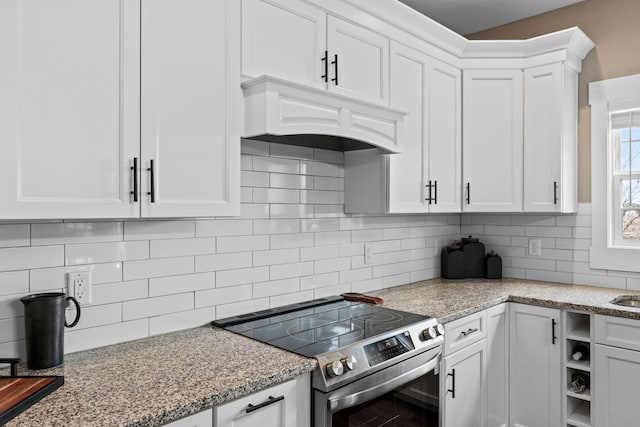 kitchen with light stone countertops, custom exhaust hood, electric range, white cabinets, and backsplash