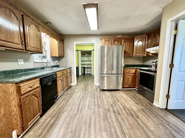 kitchen with a sink, light wood-style floors, under cabinet range hood, appliances with stainless steel finishes, and dark countertops