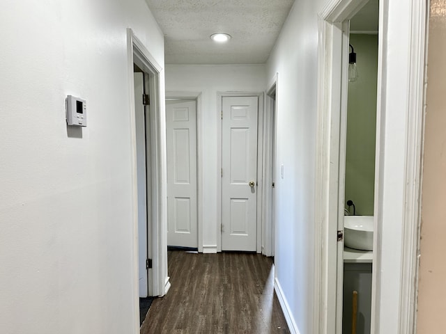 corridor featuring baseboards, a textured ceiling, and dark wood-style flooring