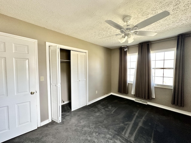 unfurnished bedroom with visible vents, a closet, dark colored carpet, baseboards, and ceiling fan