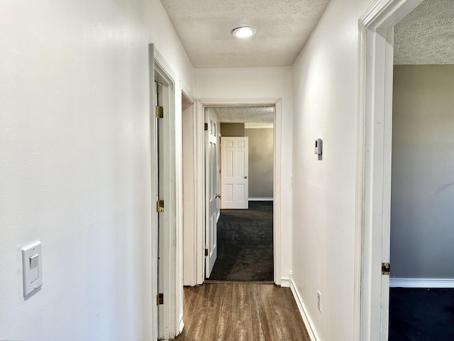 hallway with dark wood-style floors, a textured ceiling, and baseboards