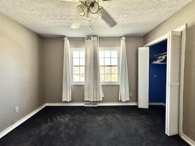 unfurnished bedroom with a textured ceiling, visible vents, dark colored carpet, and baseboards