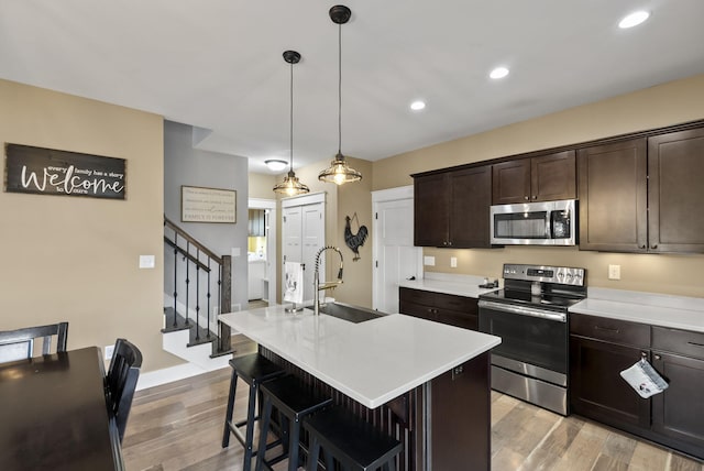 kitchen with a sink, light countertops, dark brown cabinetry, light wood-style floors, and appliances with stainless steel finishes