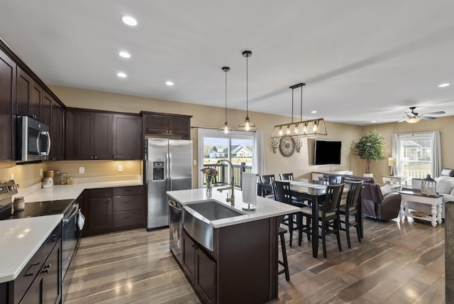 kitchen with dark brown cabinets, open floor plan, light countertops, appliances with stainless steel finishes, and wood finished floors