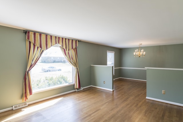 spare room featuring visible vents, wood finished floors, baseboards, and a chandelier