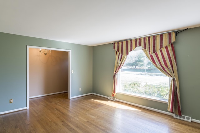 empty room with a notable chandelier, visible vents, baseboards, and wood finished floors