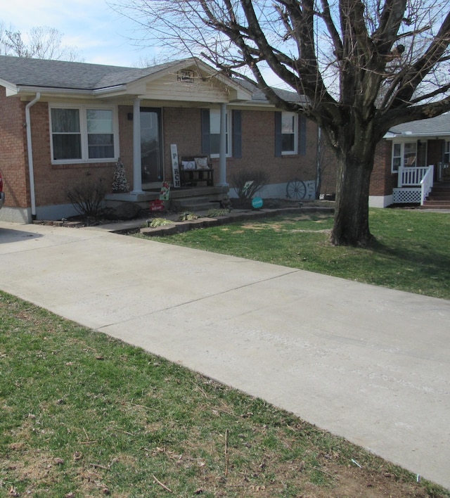 ranch-style house with a front yard, brick siding, covered porch, and roof with shingles