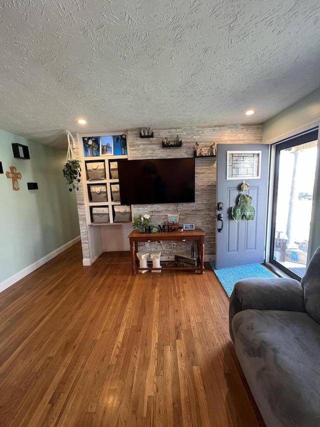 living area with baseboards, a textured ceiling, and wood finished floors