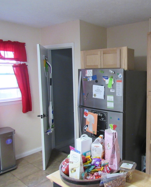 kitchen featuring light tile patterned floors, light brown cabinets, freestanding refrigerator, and baseboards