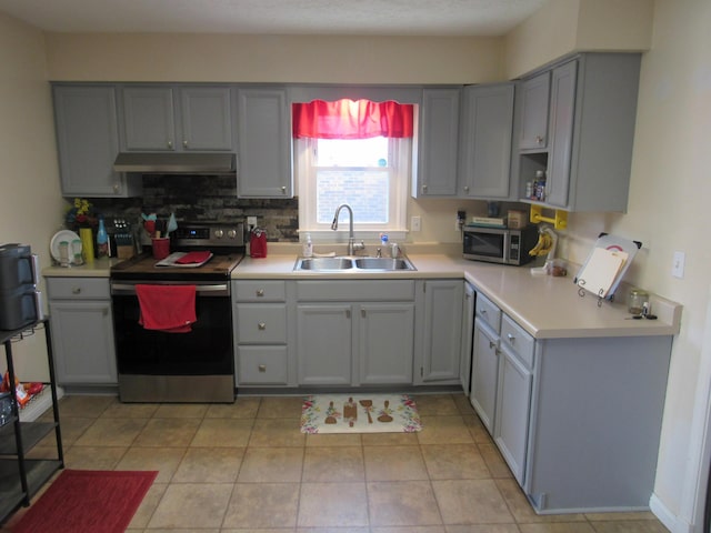 kitchen with gray cabinetry, a sink, under cabinet range hood, appliances with stainless steel finishes, and light countertops