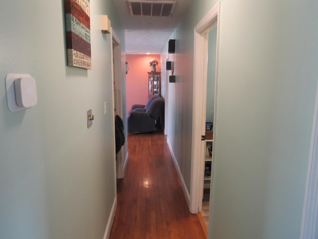 hall with visible vents, baseboards, and wood-type flooring