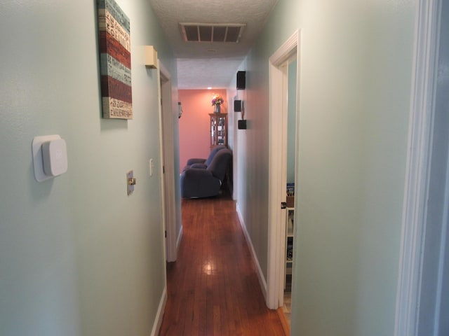 hallway with baseboards, wood finished floors, visible vents, and a textured ceiling