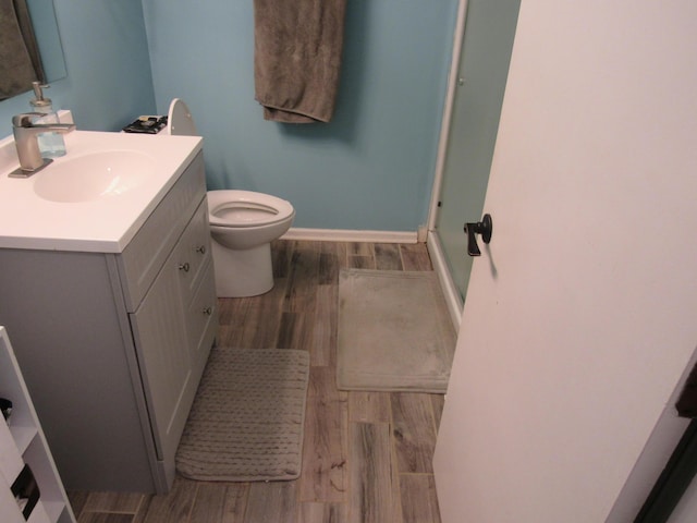 bathroom with a shower with shower door, toilet, wood finished floors, baseboards, and vanity