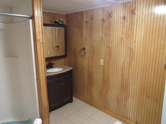 full bath featuring tile patterned floors, wooden walls, vanity, and walk in shower