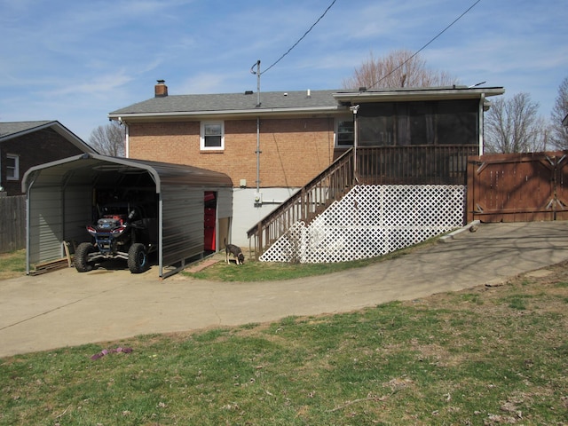 back of property with a chimney, concrete driveway, a sunroom, a carport, and brick siding