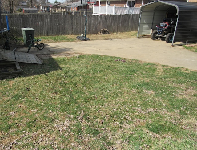 view of yard with a detached carport, concrete driveway, and fence