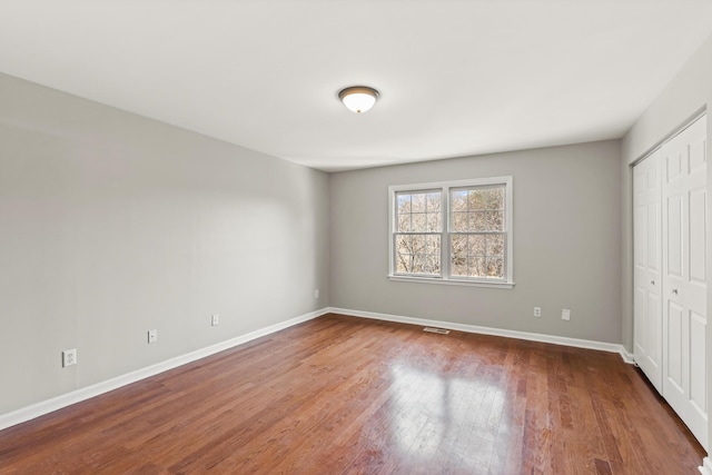 unfurnished bedroom featuring a closet, visible vents, baseboards, and wood finished floors