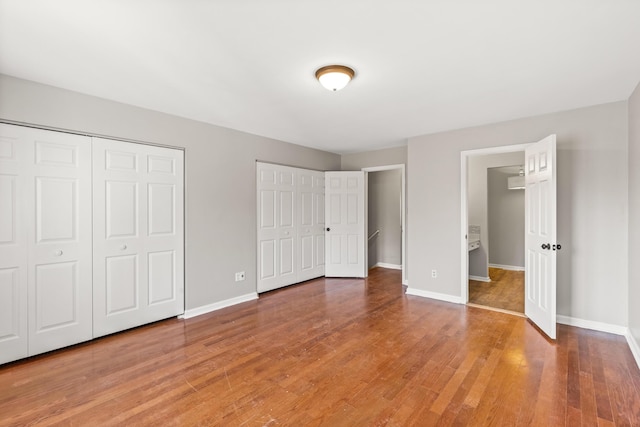 unfurnished bedroom with two closets, baseboards, and wood finished floors