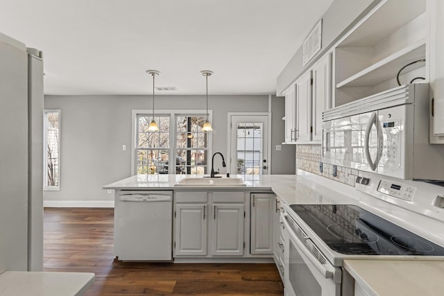 kitchen with visible vents, open shelves, a peninsula, white appliances, and a sink