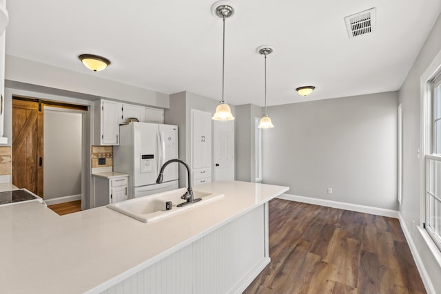 kitchen with visible vents, a peninsula, a sink, hanging light fixtures, and white refrigerator with ice dispenser