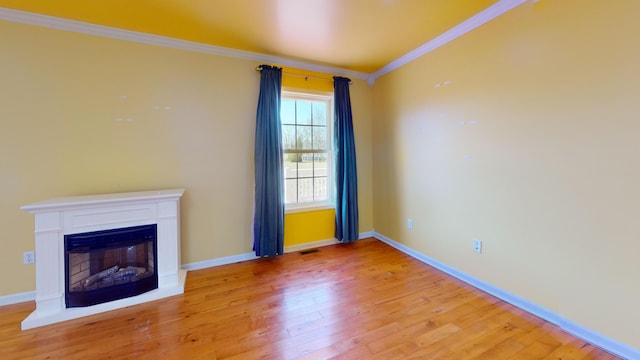 unfurnished living room featuring visible vents, ornamental molding, light wood-style flooring, a glass covered fireplace, and baseboards