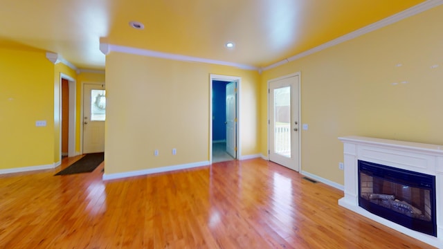 unfurnished living room with a healthy amount of sunlight, visible vents, ornamental molding, a glass covered fireplace, and light wood-type flooring