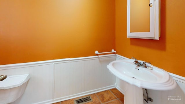 bathroom with a sink, visible vents, tile patterned flooring, and wainscoting