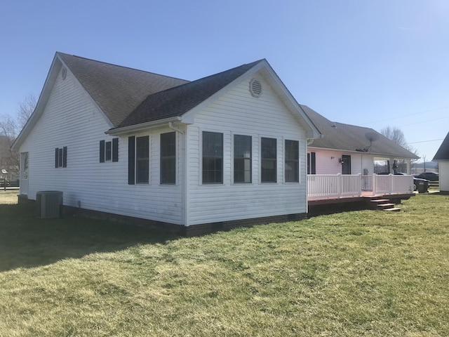 rear view of property with a lawn, central AC unit, a deck, and roof with shingles