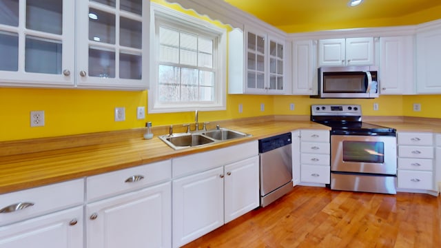 kitchen with light wood-style flooring, a sink, white cabinetry, stainless steel appliances, and glass insert cabinets