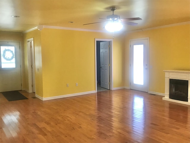 unfurnished living room featuring wood finished floors, a healthy amount of sunlight, a glass covered fireplace, and ornamental molding