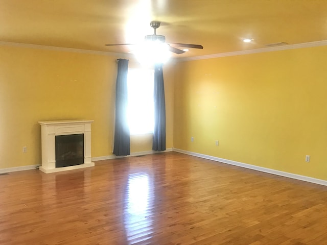 unfurnished living room with a glass covered fireplace, crown molding, wood finished floors, and ceiling fan