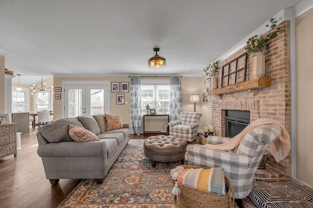 living area with a chandelier, a brick fireplace, crown molding, and wood finished floors