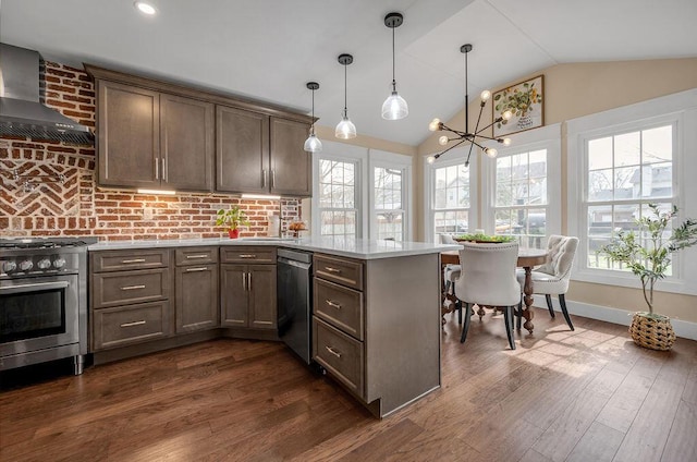 kitchen featuring lofted ceiling, a peninsula, light countertops, appliances with stainless steel finishes, and wall chimney range hood