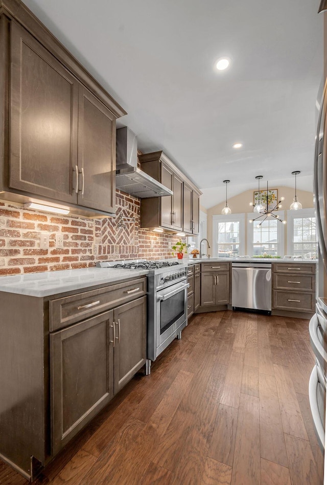 kitchen with dark wood-type flooring, light countertops, lofted ceiling, appliances with stainless steel finishes, and wall chimney exhaust hood