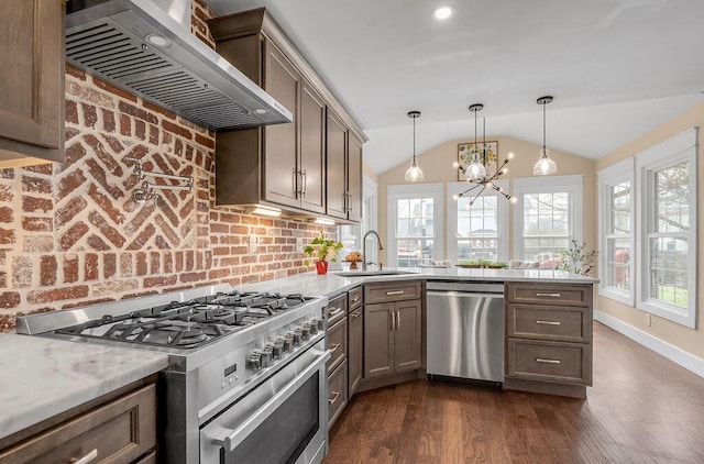 kitchen with vaulted ceiling, a peninsula, stainless steel appliances, wall chimney exhaust hood, and a sink