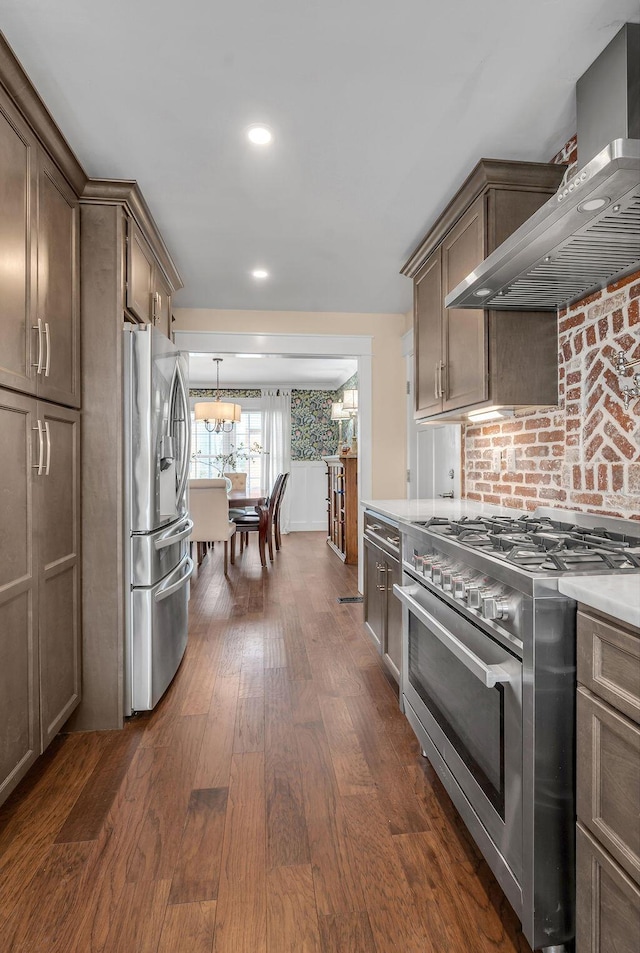 kitchen featuring wall chimney range hood, dark wood finished floors, light countertops, appliances with stainless steel finishes, and an inviting chandelier