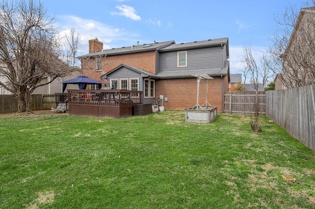 rear view of house with a fenced backyard, a yard, a wooden deck, brick siding, and a chimney