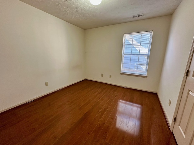 spare room with visible vents, a textured ceiling, baseboards, and wood finished floors