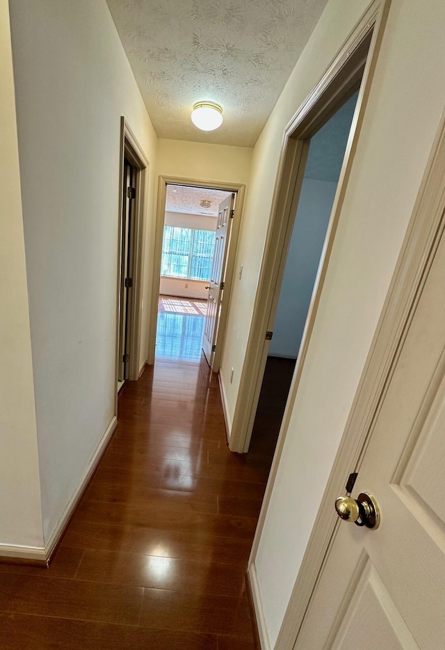 hall featuring baseboards, dark wood-style flooring, and a textured ceiling