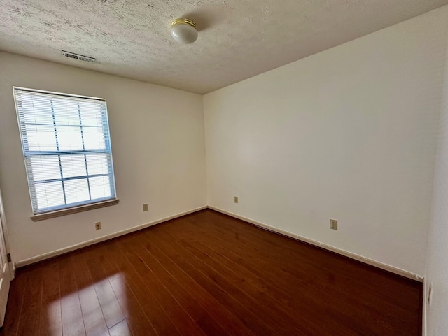 empty room featuring dark wood finished floors, visible vents, a textured ceiling, and baseboards