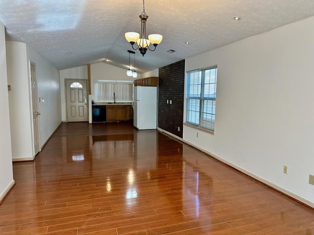 unfurnished living room with lofted ceiling, a textured ceiling, wood finished floors, an inviting chandelier, and baseboards