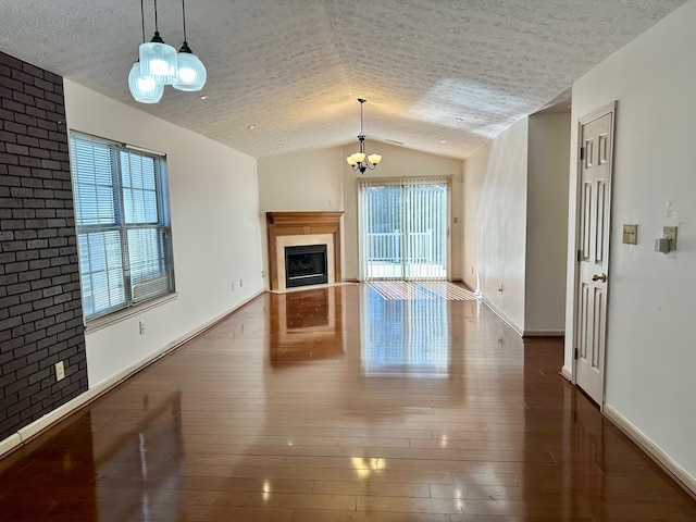 unfurnished living room featuring brick wall, a fireplace, vaulted ceiling, wood-type flooring, and a textured ceiling